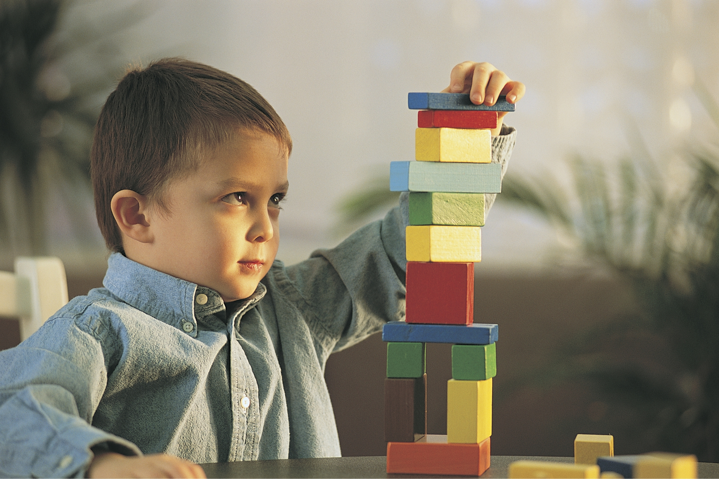 Un niño de camisa celeste apila bloques de colores en una torre alta sobre una mesa