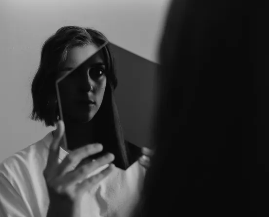 Retrato en blanco y negro de una persona sosteniendo un espejo que refleja parte de su rostro