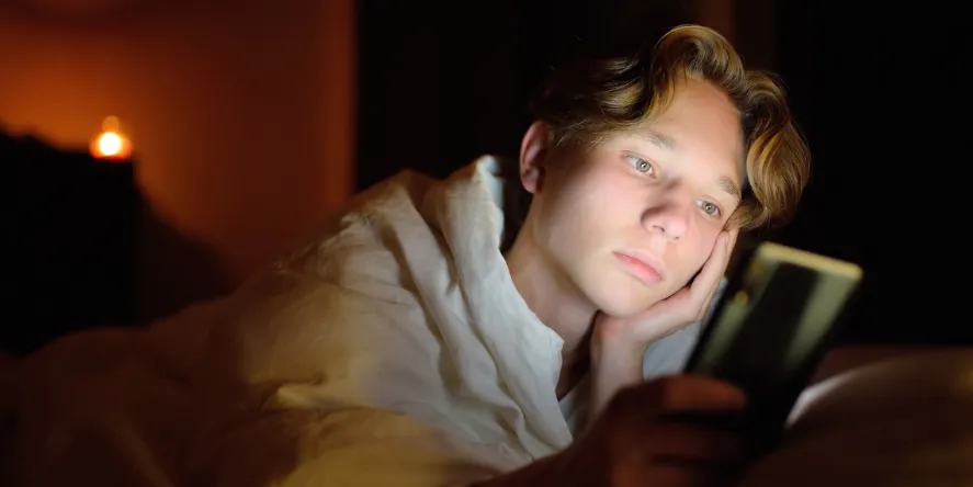 Adolescente acostado a oscuras, con la cara iluminada por la pantalla del celular