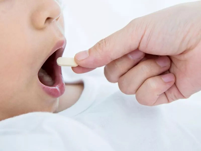 Mano de un adulto dándole una pastilla en la boca a un niño