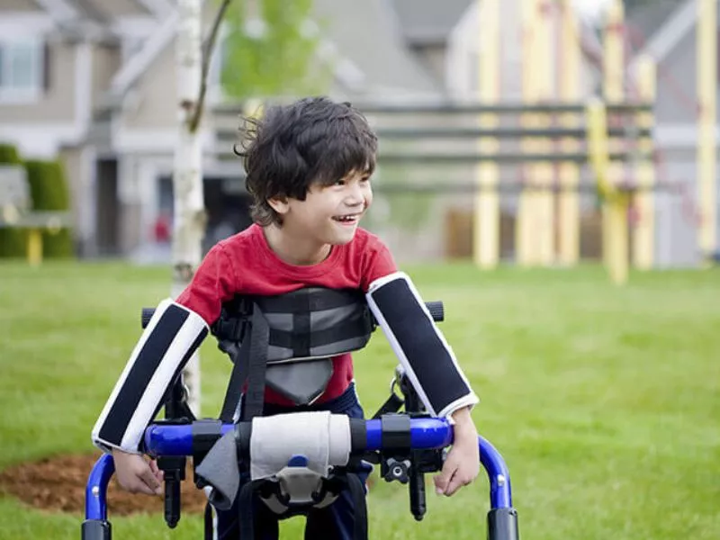 Niño sonriente caminando con un andador sobre el pasto de un parque