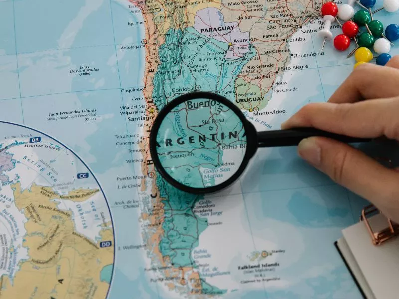 Mano sosteniendo una lupa sobre el mapa de Argentina