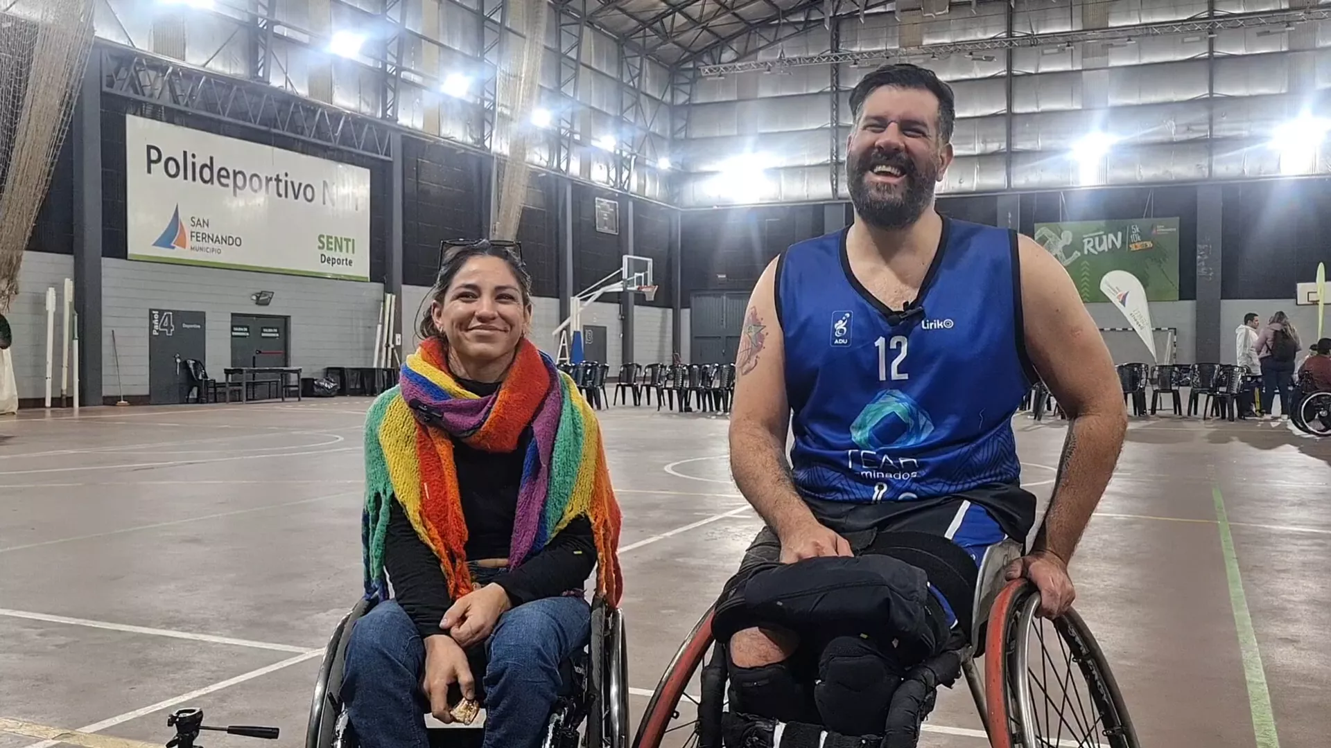 Jazmín Sallis y Cristian Gómez sonriendo en sus sillas de ruedas deportivas en un estadio de básquet