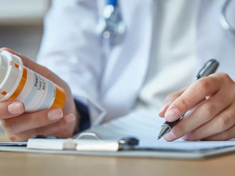 Médico con guardapolvo escribiendo una receta junto a un frasco de medicamentos