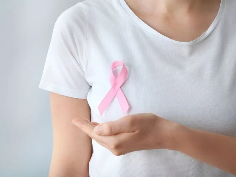 Mujer con remera blanca y un lazo rosa en el pecho, símbolo de la lucha contra el cáncer de mama