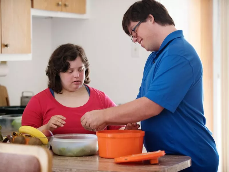 Dos jóvenes con síndrome de Down cocinando juntos en la cocina de una casa