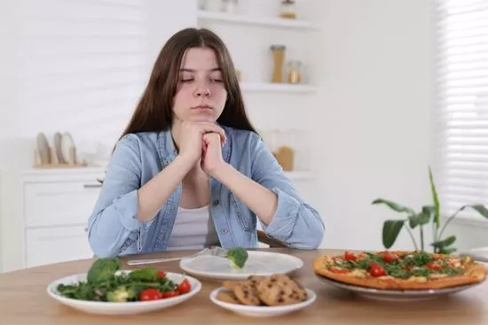 Adolescente con los ojos cerrados frente a una mesa con varios platos de comida