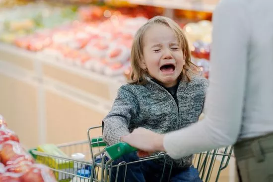 Niño llorando en el carrito del supermercado mientras un adulto lo sostiene del brazo