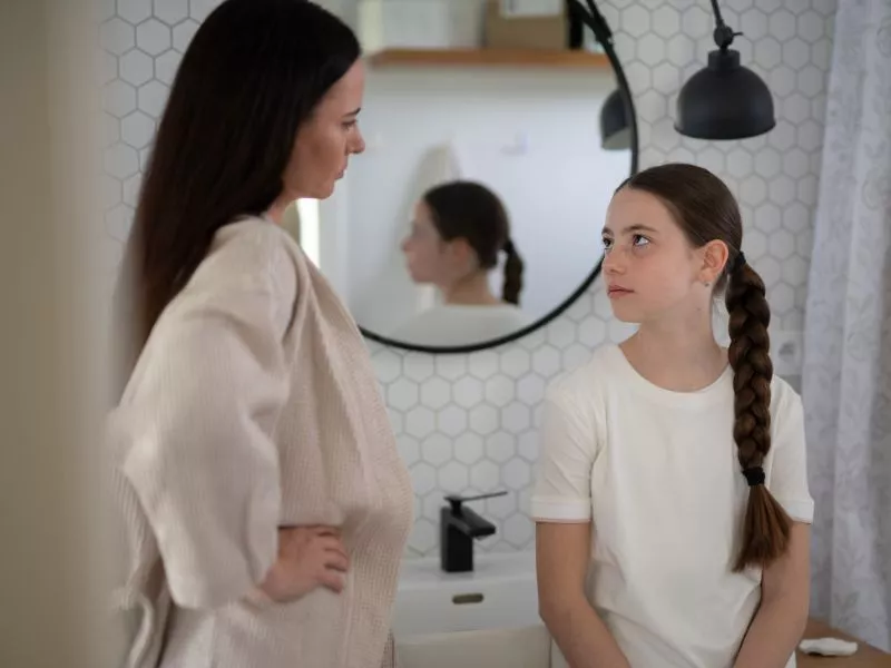 Mujer conversando con una niña en el baño de su casa, frente a un espejo