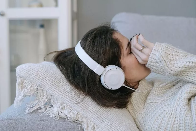 Mujer acostada en un sillón con auriculares, cubriéndose la cara con la mano